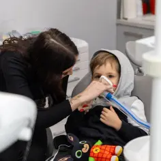 Dziecko w masce znieczulającej u dentysty, trzymanej przez kobietę.