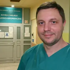 Lekarz w zielonym fartuchu stoi przed drzwiami kliniki urazowo-ortopedycznej.