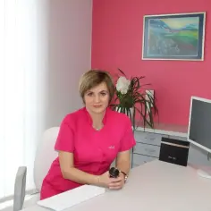 Lekarka w gabinecie dermatologicznym, siedzi przy biurku z komputerem.