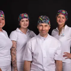 Zespół stomatologów w kolorowych czepkach i białych uniformach na czarnym tle.