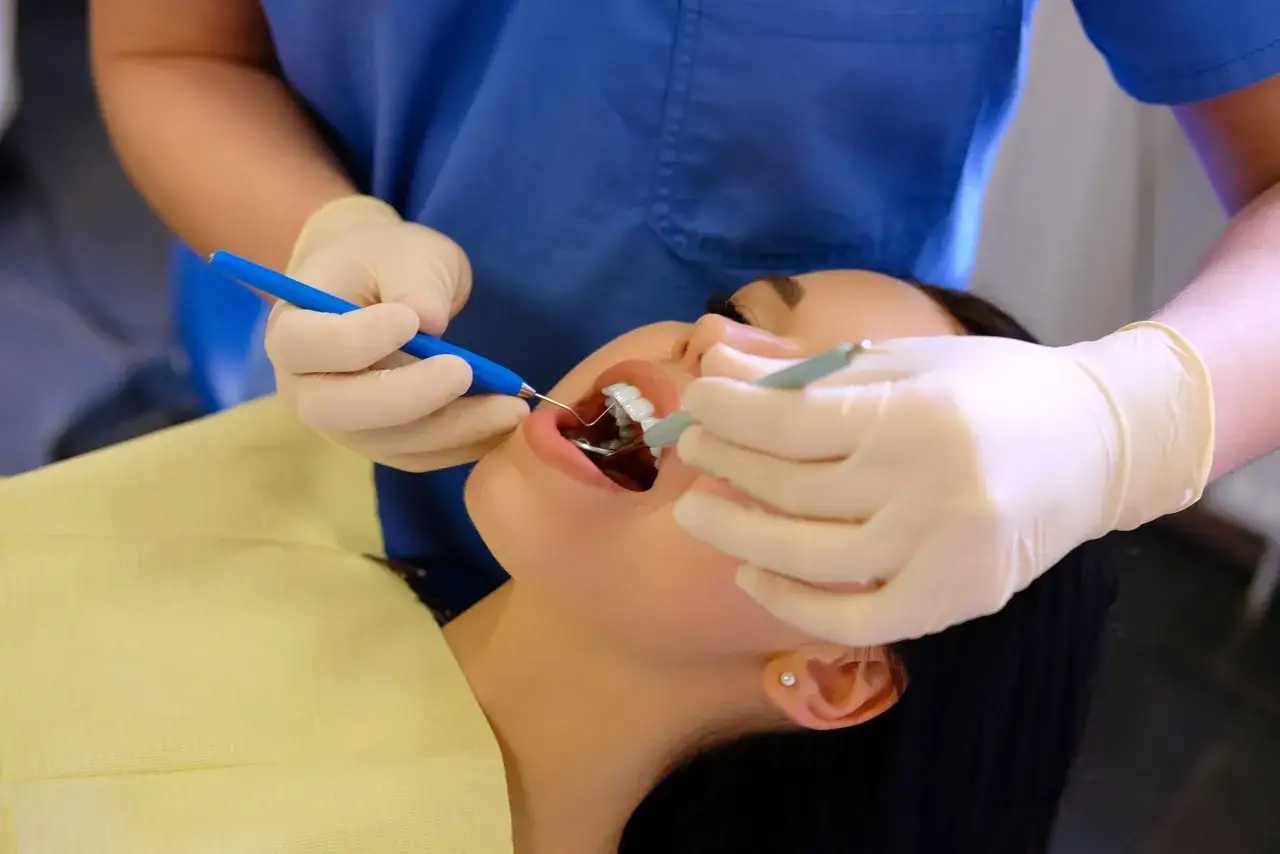Dentysta w białych rękawiczkach wykonuje zabieg szynowania zębów u pacjentki.